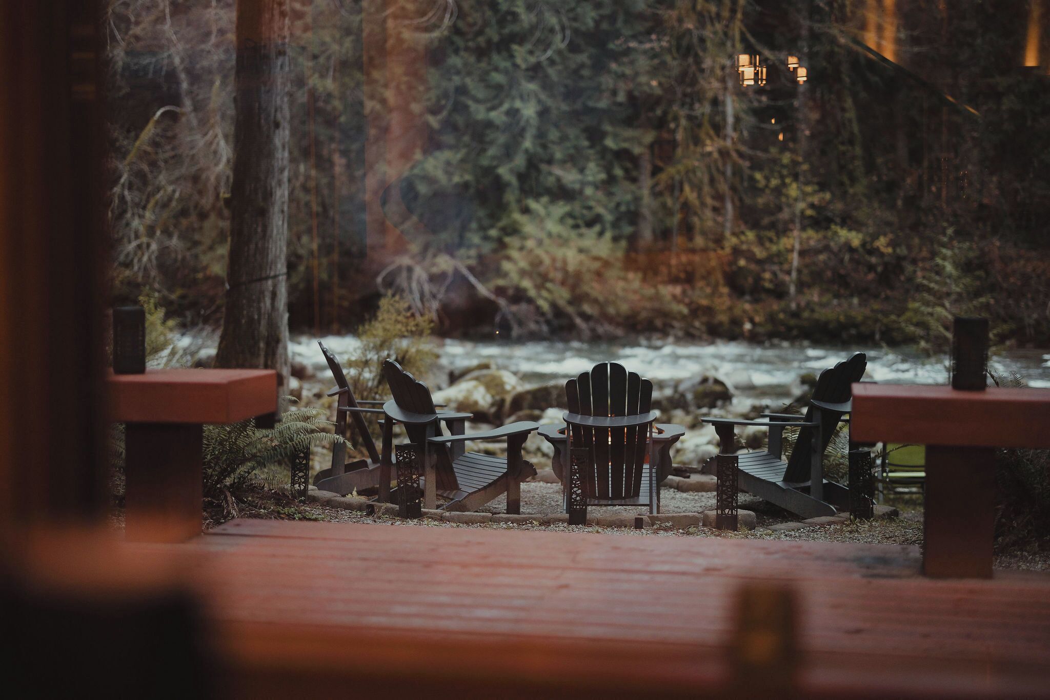 A wooden deck with Adirondack chairs and a table, overlooking a river and forested area.