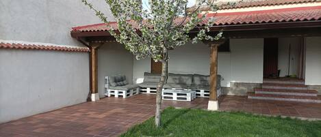 A patio area with a small tree, a grey sofa, and a white bench.