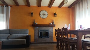 A living room with a fireplace, a sofa, a dining table with chairs, and a wall clock. - House with large garden and fireplace, ideal for families, pet friendly. (Narros de Cuéllar)