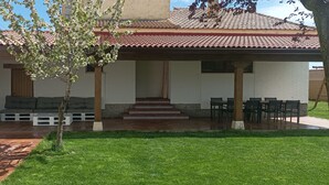 A covered patio with a seating area, a small tree, and a brick pathway leading to a building with a tiled roof. - House with large garden and fireplace, ideal for families, pet friendly. (Narros de Cuéllar)
