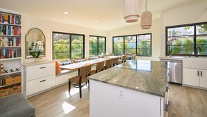 A modern kitchen with a large island, built-in bookshelves, and large windows offering views of greenery. - Breathtaking Private Beach Getaway (Ventura)