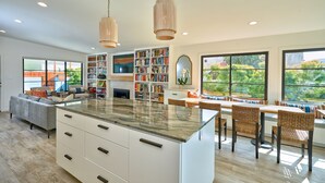 A spacious kitchen with a central island, built-in bookshelves, and a dining area with wicker chairs. - Breathtaking Private Beach Getaway (Ventura)