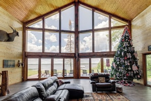 Une pièce spacieuse avec une grande fenêtre, un sapin de Noël, des meubles en cuir et une vue sur l’extérieur.