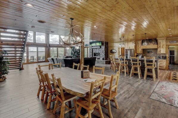 A spacious dining area with wooden tables and chairs, a fireplace, and a kitchen with wooden cabinets and a stone accent wall.