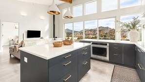 A modern kitchen with dark cabinetry, a large island, and a view of a mountainous landscape. - Spectacular Smith Rock Views on 5 Acres - Quiet and Modern w/ King Beds (Terrebonne)