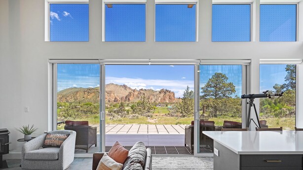 A modern living room with a sofa, armchair, and dining area, featuring large windows and a view of a mountainous landscape. - Spectacular Smith Rock Views on 5 Acres - Quiet and Modern w/ King Beds (Terrebonne)