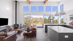 A modern living room with a fireplace, a large TV, and a sofa. There is a kitchen area with a large island and a view of the mountains. - Spectacular Smith Rock Views on 5 Acres - Quiet and Modern w/ King Beds (Terrebonne)