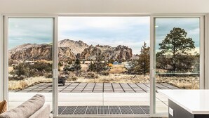 A modern room with large glass doors leading to a patio with a view of rocky mountains and sparse vegetation. - Spectacular Smith Rock Views on 5 Acres - Quiet and Modern w/ King Beds (Terrebonne)