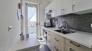 Uma cozinha moderna com armários brancos, uma pia de aço inoxidável e um micro-ondas.
