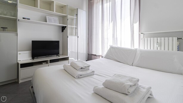 Quarto de hotel com cama, televisão e prateleira com uma moldura.