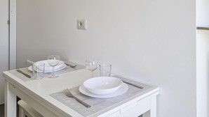 Uma área de refeições limpa e minimalista, com uma mesa branca posta para dois, incluindo pratos, copos e talheres.