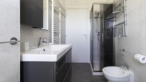 Casa de banho moderna com lavatório branco, cabine de duche em vidro e sanita.