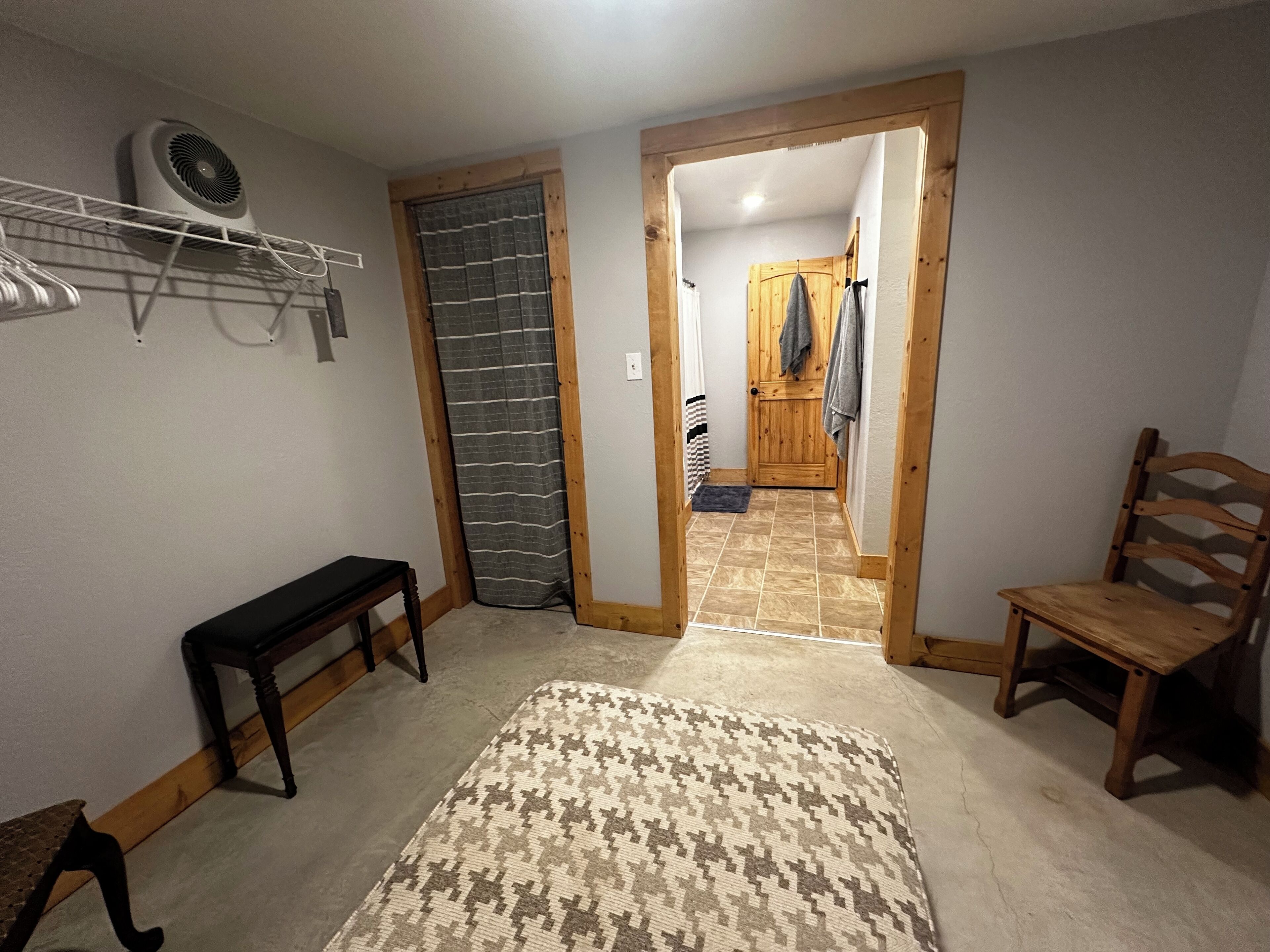 A hallway with a bench, a patterned rug, a wooden chair, a coat rack, and a door leading to another room.