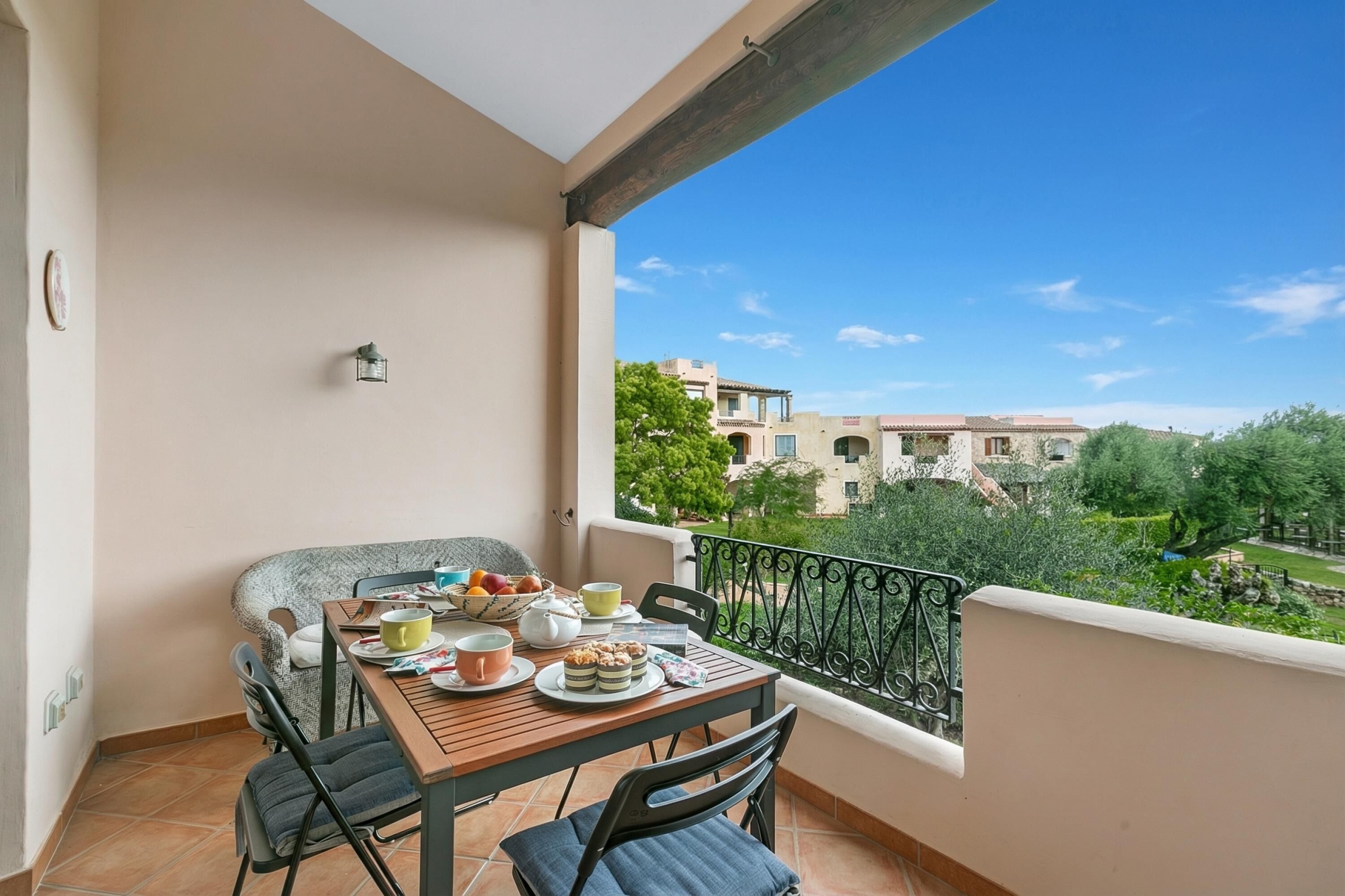 A balcony with a table set for two, a chair, and a view of buildings and trees.