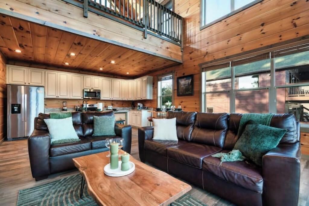 A spacious living area with two leather sofas, a wooden coffee table, and a kitchen in the background.