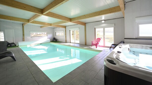A spacious indoor swimming pool with a hot tub, wooden beams, and large windows.
