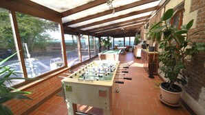 A covered outdoor area with a foosball table, brick walls, and large windows overlooking a street.