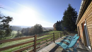A wooden deck with blue lounge chairs and a wooden fence overlooking a green landscape.