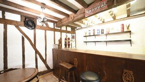 A rustic bar area with wooden beams, a sign reading "SALON," and a shelf with various bottles and glasses.