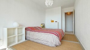A bedroom with a bed, a white dresser, a shelf with a white vase, and a hanging light fixture. - Beautiful bright apartment, exceptional view (Vallauris)