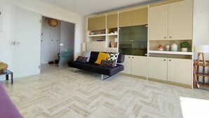 A modern living room with a sofa, herringbone-patterned flooring, and built-in storage units. - Beautiful bright apartment, exceptional view (Vallauris)
