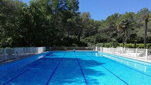 A clear blue swimming pool with white tiled edges, surrounded by a white fence and trees. - Beautiful bright apartment, exceptional view (Vallauris)
