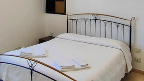 A neatly made bed with a metal frame, a small bedside table, and a wall-mounted shelf.