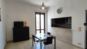 A compact kitchen with a dining area, a black TV stand, and a clock on the wall.