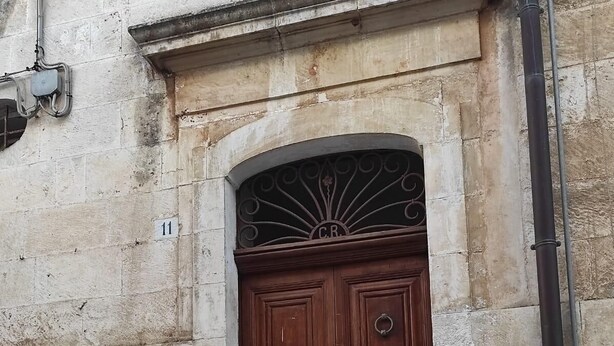 A wooden double door with a metal decorative architrave, set in a stone building with a small step leading up to it.