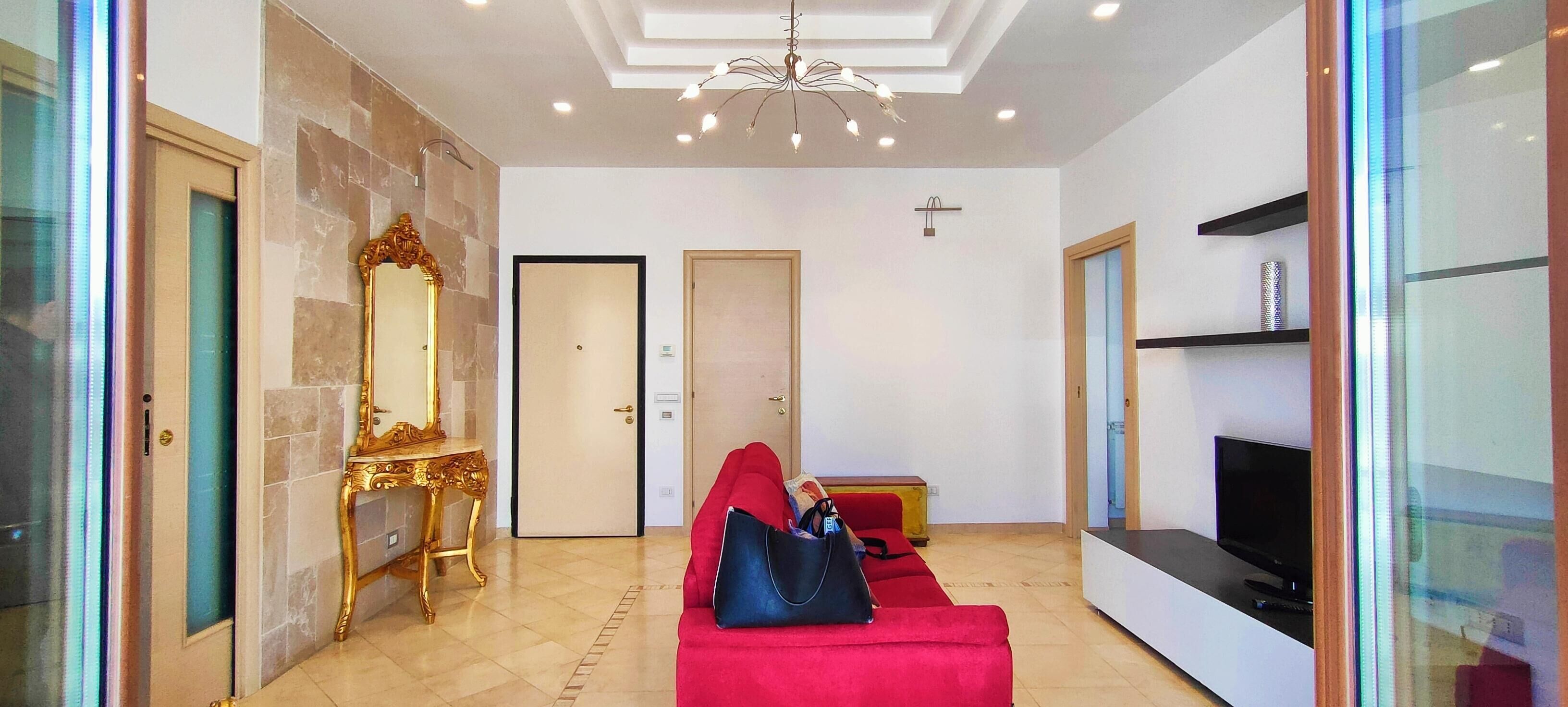 Eine Hotelhalle mit einem roten Sofa, einem Fernseher, einem goldenen, verzierten Tisch und einer Chandelüster.
