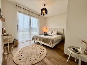 Une chambre à coucher avec un lit, une table de chevet, une lampe et une vue sur l’extérieur.