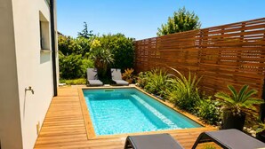 Une piscine rectangulaire avec une terrasse en bois, des chaises longues et des plantes en pot.
