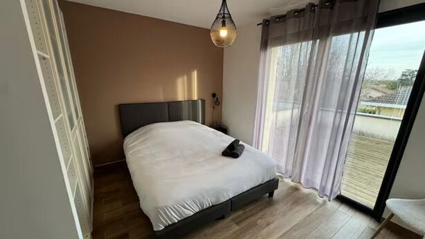 Une chambre à coucher avec un lit, une table de chevet, une fenêtre avec des rideaux et une vue sur l’extérieur.