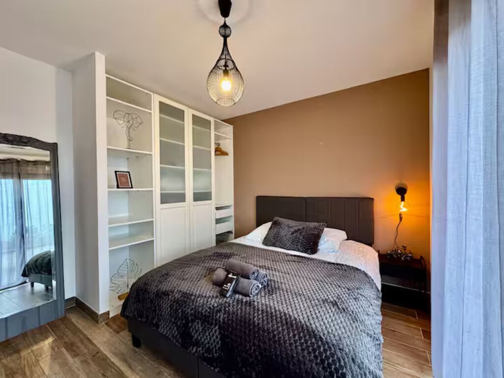 A bedroom with a bed, a wardrobe, a bedside table, and a hanging light fixture.