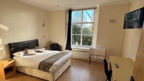 A bedroom with a bed, a desk, a chair, a radiator, and a window with curtains.
