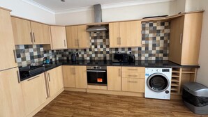 A compact kitchen with wooden cabinets, a black countertop, a built-in oven, a washing machine, and a tiled backsplash.