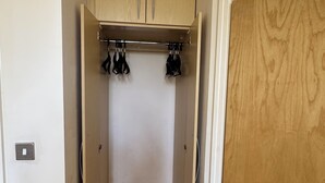 A narrow hallway with a wooden door on the right, a beige wardrobe with two doors, and a coat rack with black items.