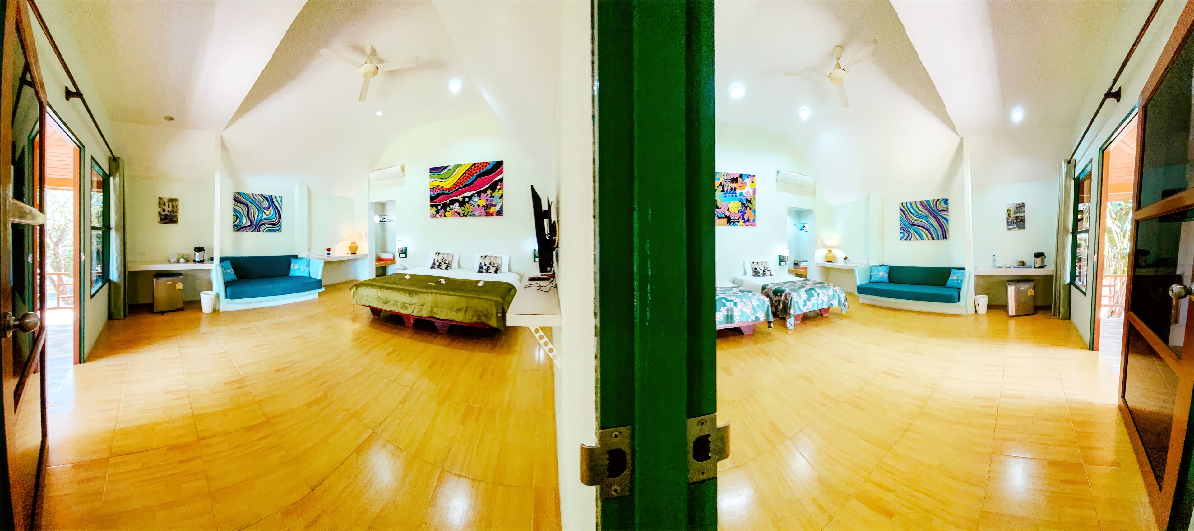 Um quarto amplo com piso de madeira, um sofá verde, uma cama com roupa de cama floral e arte abstrata colorida nas paredes.