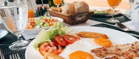 A breakfast setting with a plate of eggs, sausages, and tomatoes, a basket of bread, and a glass of orange juice.
