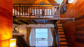 Interior de madera con un balcón identificado como “Balcón”, una escalera y vista al mar a través de una puerta.