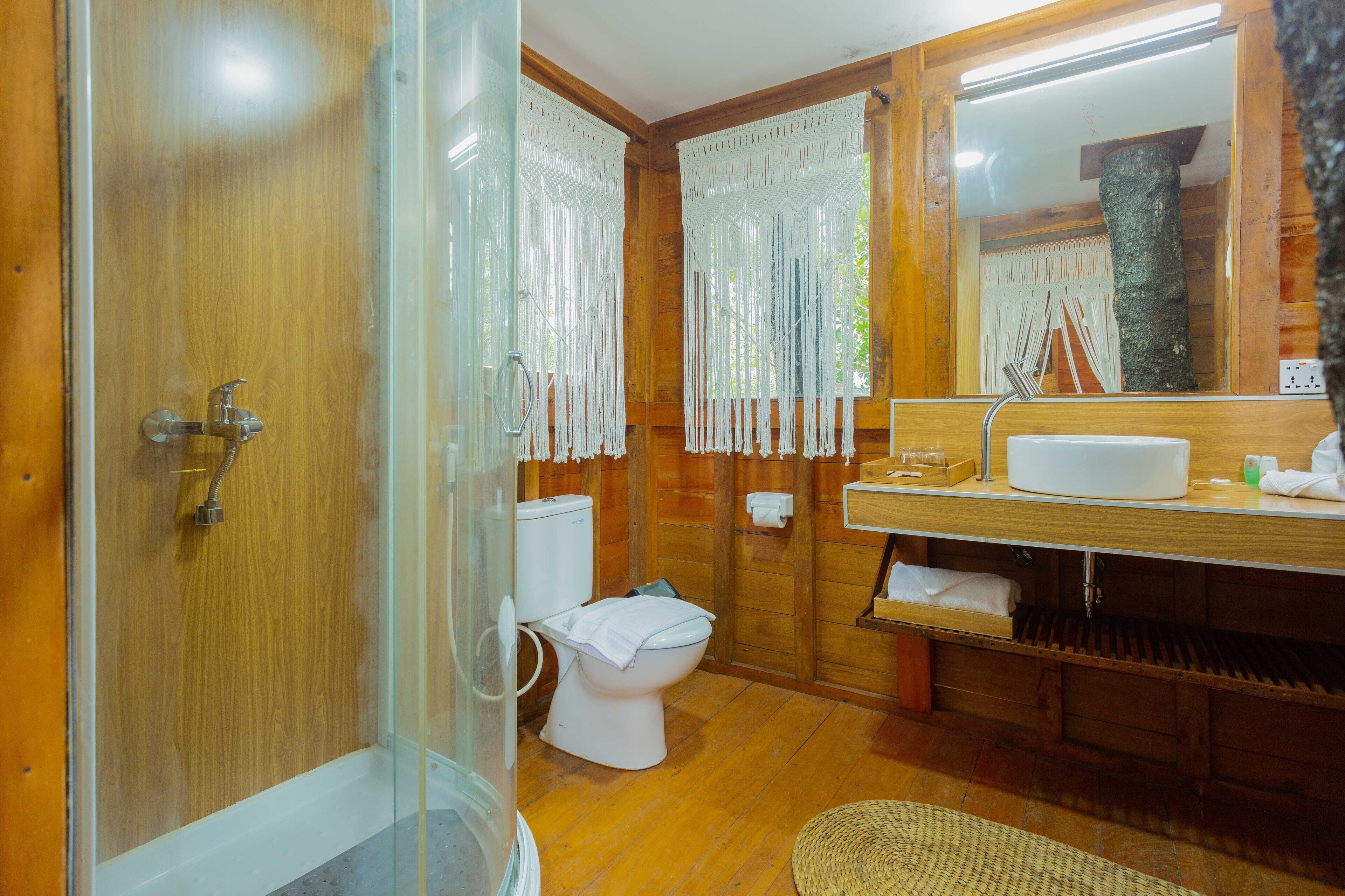 A wooden bathroom with a glass shower enclosure, a white toilet, and a wooden vanity with a mirror and sink.