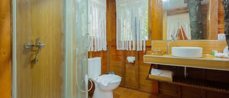 A wooden bathroom with a glass shower enclosure, a white toilet, and a wooden vanity with a mirror and sink.