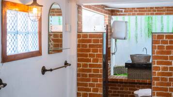 A bathroom with a brick wall, a white door, a window with a diamond-patterned glass, a white sink, and a white toilet.