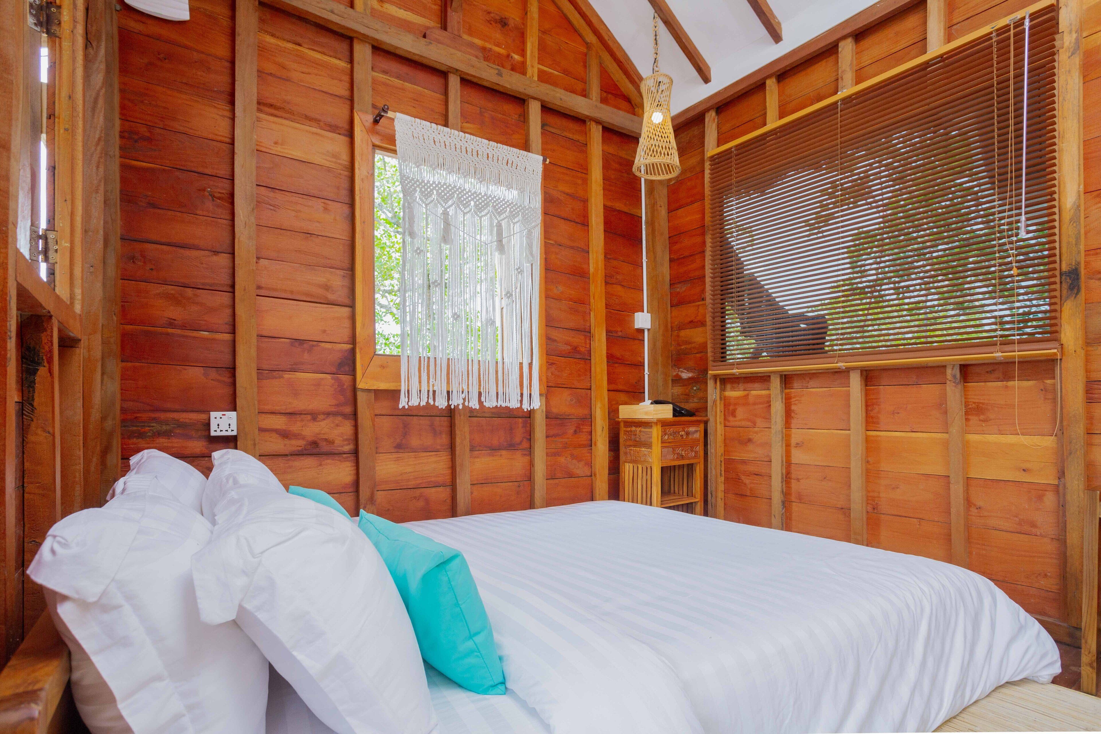 Dormitorio de una cabaña de madera con cama, cortinas blancas y una lámpara colgante.