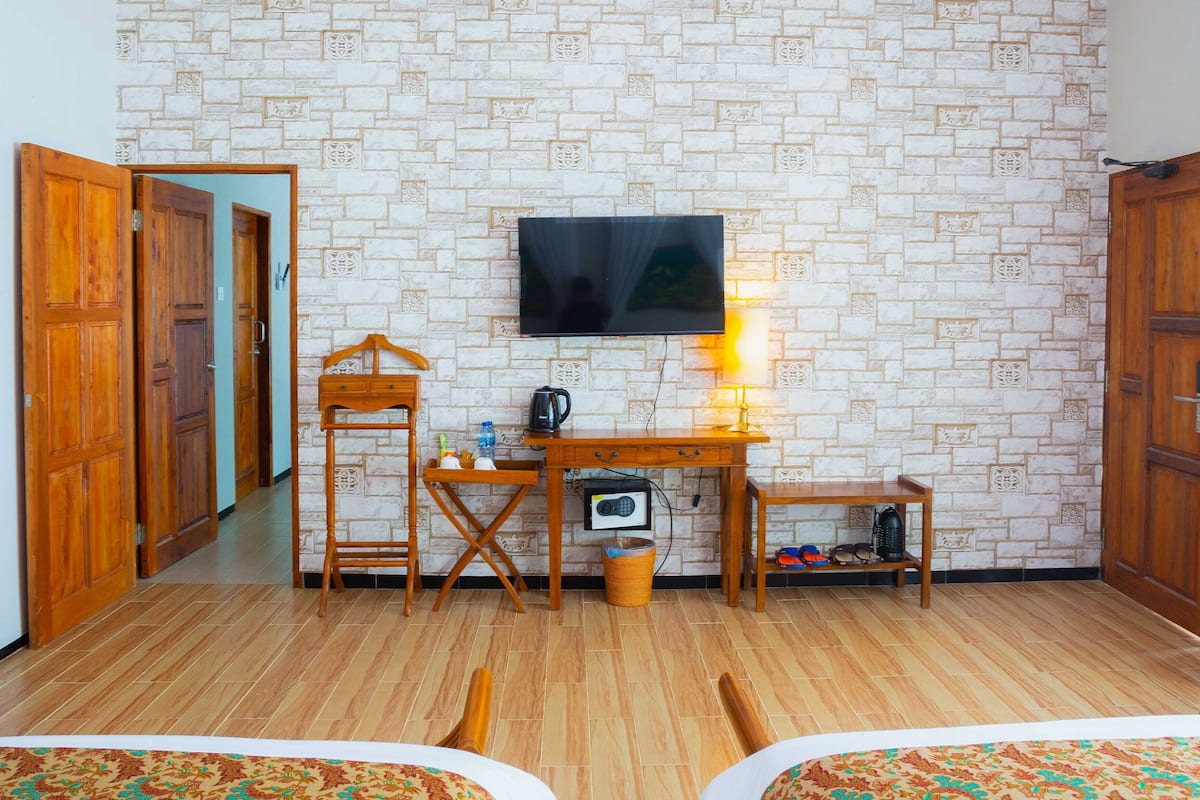 Ett hotellrum med två sängar, en TV, ett skrivbord med en stol och en vägg med ett mönster som efterliknar tegelstenar.