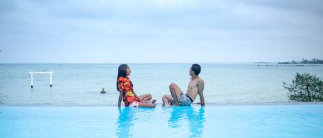 Two people sitting by a pool with a view of the sea.
