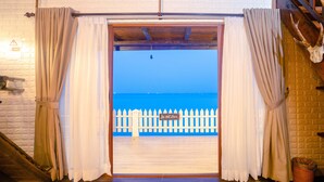 Una puerta con cortinas color crema, cerca blanca enrejada y vista al mar.