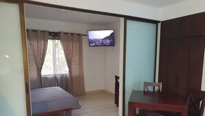 Ein Zimmer mit einem Bett, einem an der Wand befestigten Fernseher, einem Esstisch mit Stühlen und einer Schiebetür.