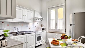 A modern kitchen with white cabinets, a stove, a microwave, and a dining area with a table set for a meal. - Central apartment Stella House (Massa Lubrense)