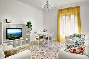 A living room with a TV, white furniture, a chandelier, and a yellow curtain.